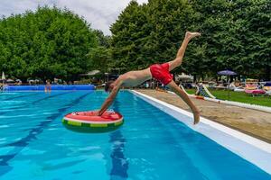 young man in swimsuit playfully diving from the edge of a swimming pool into a round lifebuoy photo