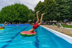 young man in swimsuit playfully diving from the edge of a swimming pool into a round lifebuoy photo