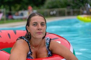portrait of young woman in swimsuit inside big red lifebuoy in swimming pool during summer vacation photo
