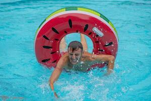 young man in swimsuits having fun in the splashing blue water of a swimming pool inside a red and green inflatable photo