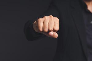 A businessman in a black suit raises his fist to the front, showing determination, and encouragement while standing on a black background photo