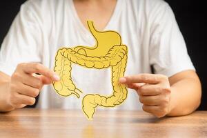 Hand holding a large intestine shape made from paper while sitting over a black background photo