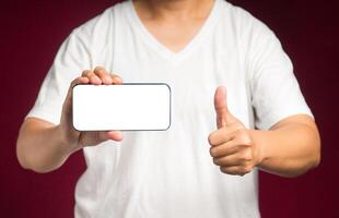 Hand holding a horizontal mobile phone with a blank white screen and showing thumbs up while standing on a red background photo