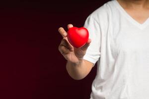 Close-up of hand holding a red heart shape while standing on a red background photo