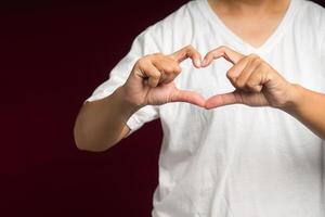 hombre en blanco casual haciendo corazón figura amor firmar con dedos mientras en pie en un rojo antecedentes foto