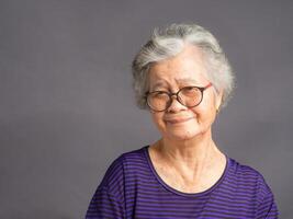 Portrait of a senior woman looking at the camera with a smile while standing over a gray background photo