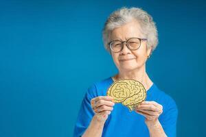 Portrait of a senior woman holding a brain mockup and looking at the camera while standing on a blue background photo