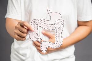 Hand holding a colon shape symbol and touching the stomach while standing on a gray background photo