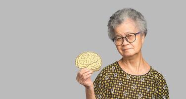 Portrait of a senior woman holding a brain symbol while standing on a gray background photo
