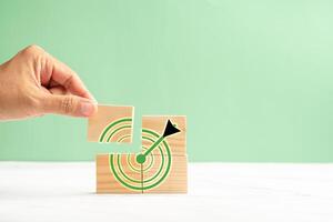 Close-up of hand holding a wooden cube with a target icon over a marble floor against a green background photo