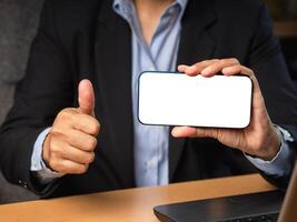 Hand holding a horizontal mobile phone with a blank white screen and showing thumbs up while sitting in the office photo