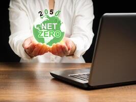 The earth icon with the letters Net-zero on the palm woman while sitting in the office photo