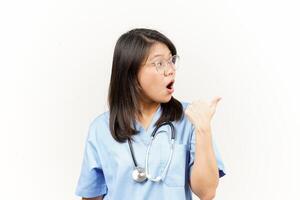 Showing and Pointing Product With Thumb Of Asian Young Doctor Isolated On White Background photo
