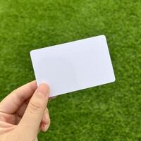 Hand holding empty copy spaced blank white card isolated on square green grass carpet background. photo