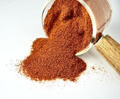 Red paprika powder food ingredients spilled from small glassware cup isolated on horizontal white background. photo