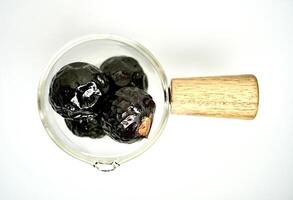 Black or dark brown colored soap berry nuts or buah lerak in small cup with wooden handle isolated on horizontal white background. photo