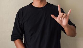 Young man showin I LOVE YOU gesture in sing language on gray background photo