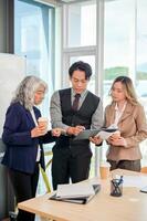Diverse Asian businesspeople stand together in a modern office, focused on discussing work. photo