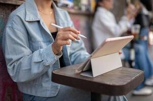 A close-up of a woman sits at an outdoor table of a cafe in the city, using her digital tablet. photo