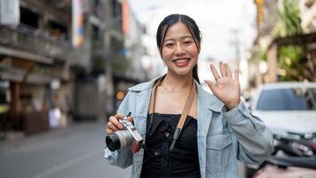 A happy Asian female tourist enjoying taking photos while exploring the city, smiling at the camera.