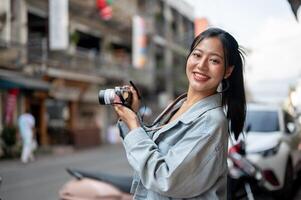 A happy Asian female tourist enjoying taking photos while exploring the city, smiling at the camera.