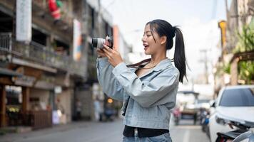 A happy Asian female tourist enjoying taking photos with her camera while exploring the city.