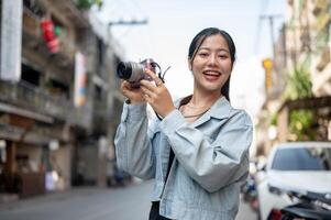 A happy Asian female tourist enjoying taking photos while exploring the city, smiling at the camera.