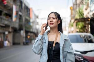 A confused female tourist talking on the phone with her taxi driver while walking down the street. photo