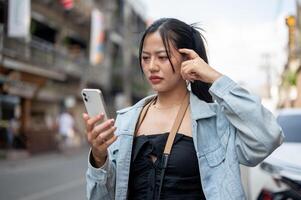 A confused Asian female tourist using her smartphone to check the direction on the map app in city. photo
