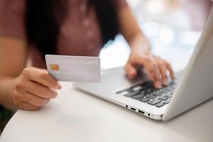 A close-up of a woman showing her credit card to the camera while using her laptop. photo