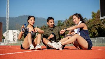 Portrait of a group of cheerful Asian athlete friends resting on a sports track after training. photo