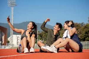 Group of athlete friends enjoying taking selfies while resting on a sports track after training. photo