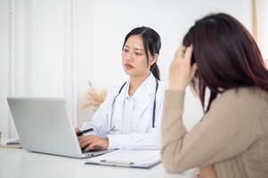 A thoughtful doctor listening to a patient's symptoms while working on her laptop in a clinic. photo