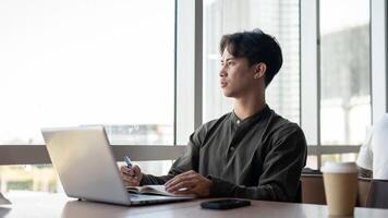 A thoughtful Asian businessman admiring the view outside with a serious expression while working. photo