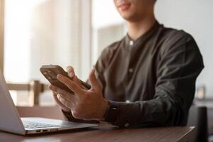 A close-up of a smiling Asian businessman using his smartphone while working in a modern office. photo