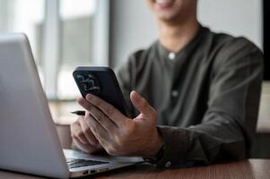 A close-up of a smiling Asian businessman using his smartphone while working in a modern office. photo