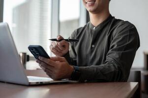 A close-up of an Asian businessman using his smartphone while working in a modern office. photo