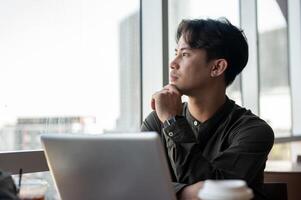 A thoughtful Asian businessman admiring the view outside with a serious expression while working. photo