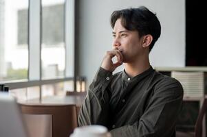 A thoughtful Asian businessman admiring the view outside with a serious expression while working. photo