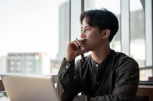 A thoughtful Asian businessman admiring the view outside with a serious expression while working. photo