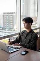 A focused businessman working in his office, writing in a book while sitting in front of a computer. photo