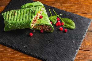 Homemade shawarma with spinach filled with chicken, vegetables on a stone board photo