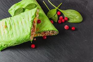 Homemade shawarma with spinach filled with chicken, vegetables on a stone board photo