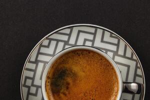 Fresh strong espresso in a silver cup on a plate on a black background, top view photo