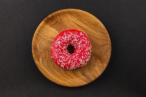 fresh delicious donut with red glaze on a wooden plate, top view photo