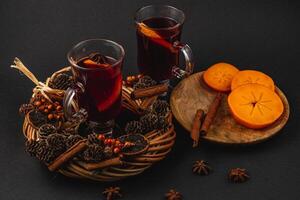 Delicious mulled wine with spices and sweet persimmons on a wooden plate photo