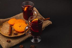 Delicious mulled wine with spices and sweet persimmons on a wooden plate photo