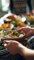 Close-up of hands passing dishes at a Thanksgiving dinner table filled with traditional foods. Concept of holiday celebration, gratitude, and sharing. Vertical photo