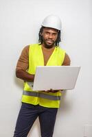 Construction worker in reflective vest using a laptop computer in front of a white wall. photo