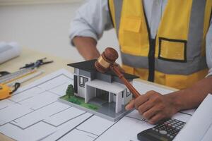 Judge gavel on building blueprint plans with a yellow safety helmet in the background. law that deals with matters relating to building construction, engineering. Construction law concept. photo